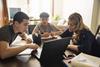 A photo of a mother helping her two teenage sons with schoolwork