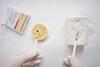 A scientist wearing disposable gloves holds indicator paper over a slice of lemon and a bar of soap