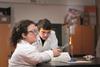 An image showing a female student burning magnesium on a Bunsen burner using tongs while a male classmate is watching the flame created. Both are wearing safety goggles