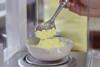 A close up of someone using a spoon to add sulfur powder to a weighing boat on top of a balance