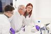 John Holman with a female and a male student, all wearing safety goggles and gloves, in a lab
