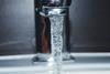 A close-up photograph of water flowing from a silver tap