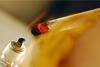 A close-up photograph of a substance being heated in a test tube over a spirit lamp
