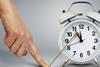 A forefinger holds down a string attached to the big hand of an alarm clock, effectively stopping time