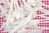 A pile of white plastic cutlery on a red and white checkered tablecloth