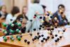 Models of different types of chemical bonding including diamond and salt on a table in a classroom. Behind a teacher speaks to the high school students.