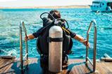 A scuba diver with an air tank sits on the edge of a boat ready to enter the ocean