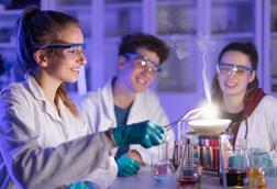 Students in protective lab clothing, working together around beakers and burning magnesium
