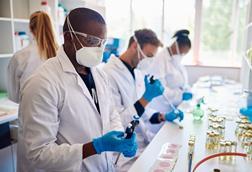 Photo of technicians wearing face masks and coats working together with samples at a table in a lab