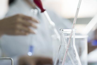 A glass thermometer resting in a glass conical flask in a laboratory setting