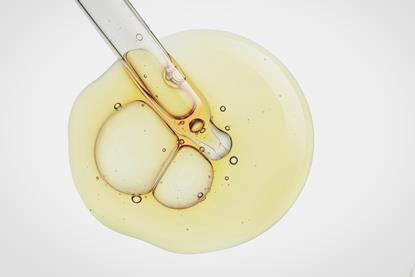 A macro photograph of a drop of pale yellow liquid and the end of a pipette on a white surface