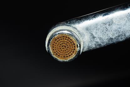 The underside of a bathroom tap coated in white and discoloured limescale deposits