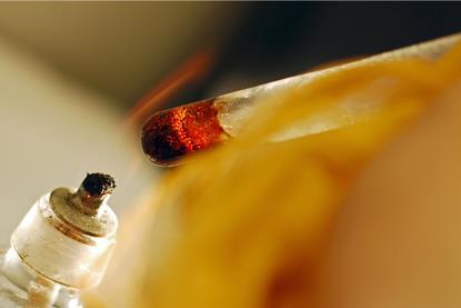 A close-up photograph of a substance being heated in a test tube over a spirit lamp