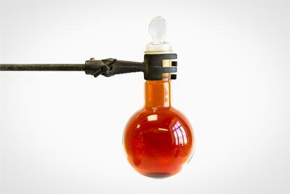 A glass flask containing bromine liquid, suspended from a metal laboratory clamp