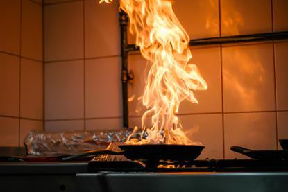 A large fire rising from a black flying pan on a kitchen stove