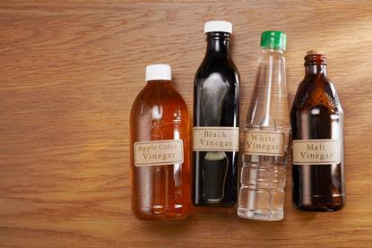 A photograph of four bottles containing different varieties of vinegar, including apple cider, black, white and malt vinegar