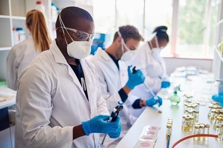 Photo of technicians wearing face masks and coats working together with samples at a table in a lab
